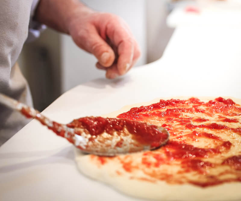 Un pizzaiolo étale de la sauce tomate sur une pate à pizza